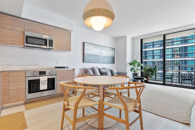 kitchen with light brown cabinetry, appliances with stainless steel finishes, breakfast area, a wall of windows, and light hardwood / wood-style floors