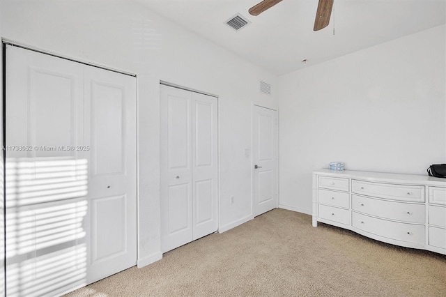 unfurnished bedroom with multiple closets, ceiling fan, and light carpet