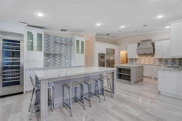 kitchen with a breakfast bar area, custom exhaust hood, a kitchen island, beverage cooler, and white cabinets