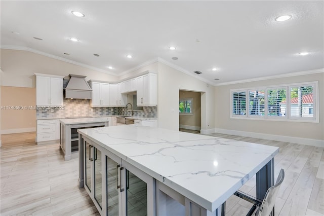 kitchen with custom exhaust hood, a kitchen island, white cabinets, and light stone counters