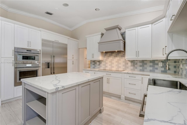 kitchen featuring premium range hood, white cabinets, a center island, light stone counters, and stainless steel appliances