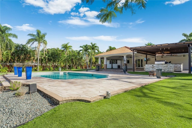 view of swimming pool featuring a yard, ceiling fan, exterior bar, exterior kitchen, and a patio