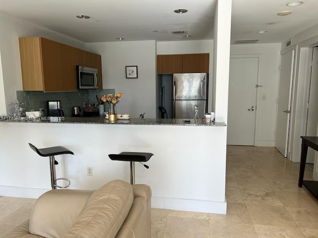 kitchen featuring a breakfast bar, appliances with stainless steel finishes, decorative backsplash, kitchen peninsula, and dark stone counters