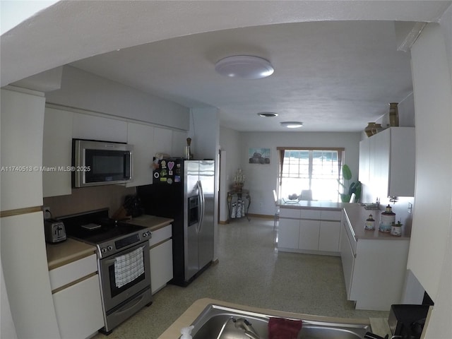 kitchen featuring light speckled floor, stainless steel appliances, light countertops, and white cabinetry