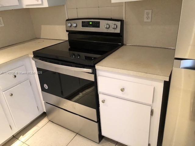 kitchen featuring white cabinets, light tile patterned floors, stainless steel range with electric cooktop, and backsplash