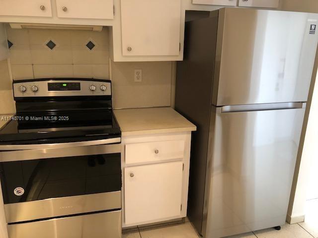 kitchen featuring tasteful backsplash, stainless steel appliances, light tile patterned floors, and white cabinets