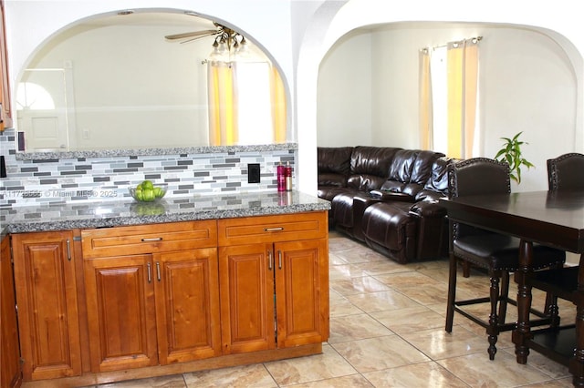 kitchen featuring decorative backsplash, ceiling fan, and stone countertops