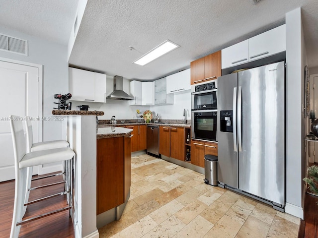 kitchen featuring wall chimney range hood, sink, appliances with stainless steel finishes, white cabinets, and dark stone counters