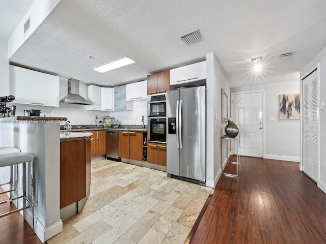 kitchen featuring white cabinetry, stainless steel appliances, a breakfast bar area, and wall chimney range hood