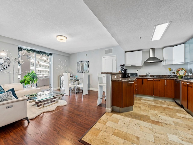 kitchen featuring white cabinets, a kitchen breakfast bar, a center island, wall chimney exhaust hood, and light hardwood / wood-style flooring