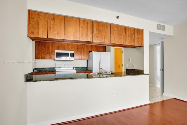 kitchen with sink, dark stone countertops, white appliances, and kitchen peninsula