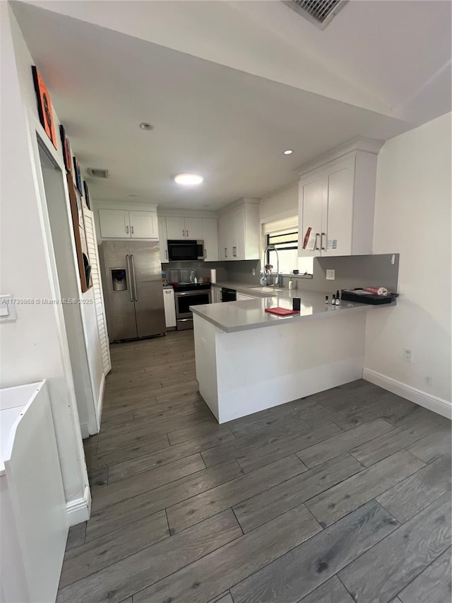 kitchen with hardwood / wood-style flooring, white cabinetry, appliances with stainless steel finishes, and kitchen peninsula