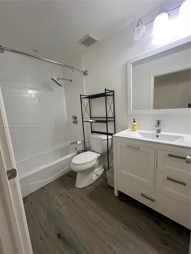 full bathroom with tiled shower / bath, decorative backsplash, hardwood / wood-style flooring, vanity, and toilet