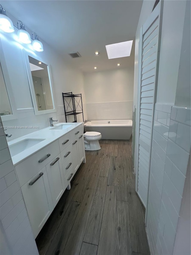 bathroom with hardwood / wood-style floors, a skylight, vanity, a washtub, and toilet