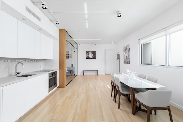 kitchen with white cabinetry, sink, light hardwood / wood-style flooring, and oven