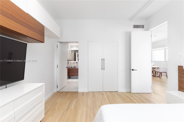 unfurnished bedroom featuring beamed ceiling, connected bathroom, light wood-type flooring, and a closet