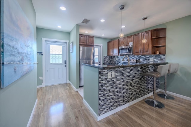 kitchen featuring appliances with stainless steel finishes, decorative light fixtures, tasteful backsplash, light hardwood / wood-style floors, and kitchen peninsula