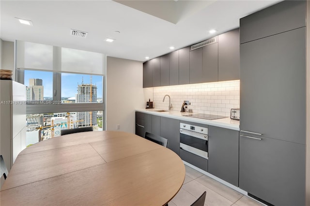 kitchen with light tile patterned flooring, gray cabinetry, stainless steel oven, black electric stovetop, and decorative backsplash