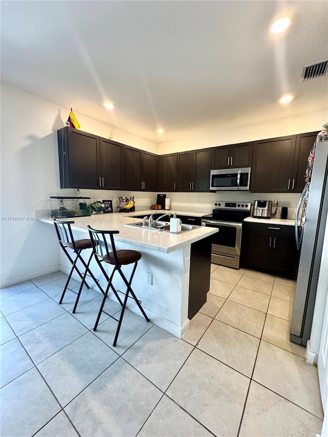 kitchen with light tile patterned flooring, appliances with stainless steel finishes, a breakfast bar, and kitchen peninsula