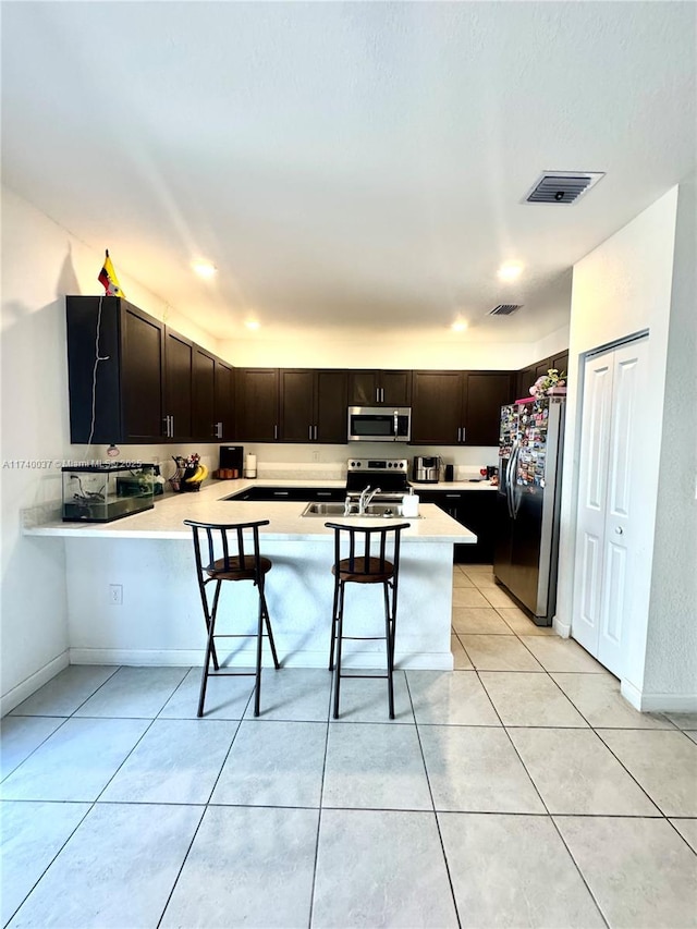 kitchen featuring appliances with stainless steel finishes, a kitchen breakfast bar, kitchen peninsula, and dark brown cabinets