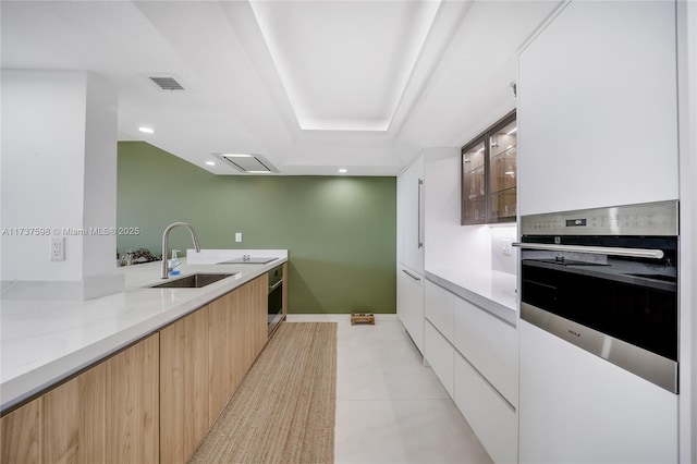 kitchen with white cabinetry, oven, sink, and light stone counters