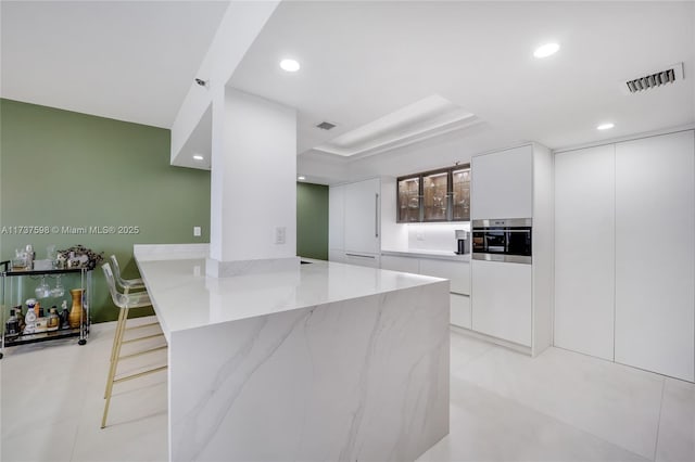 kitchen with white cabinetry, a breakfast bar, and light stone counters