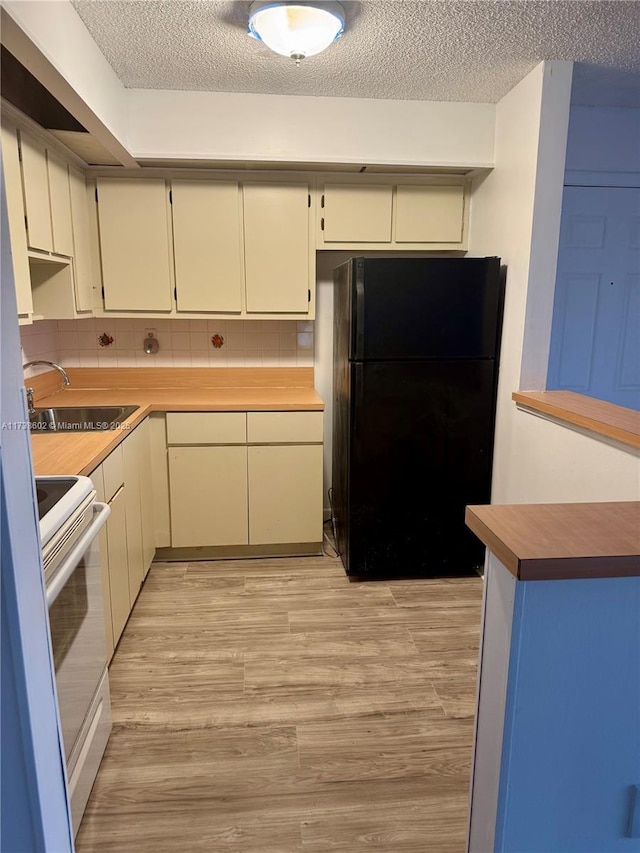 kitchen with black fridge, sink, white electric range, and cream cabinets