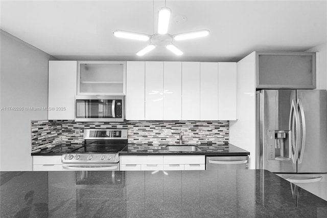 kitchen with appliances with stainless steel finishes, tasteful backsplash, white cabinetry, sink, and dark stone counters