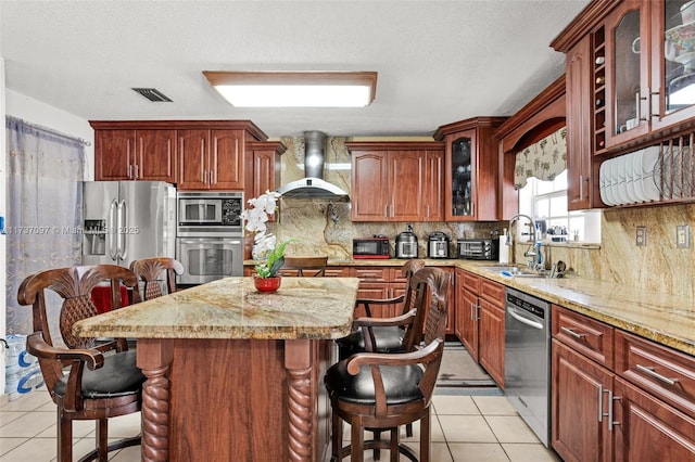 kitchen featuring sink, a center island, light tile patterned floors, appliances with stainless steel finishes, and wall chimney range hood