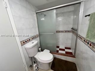 bathroom with a shower with door, tile walls, and toilet