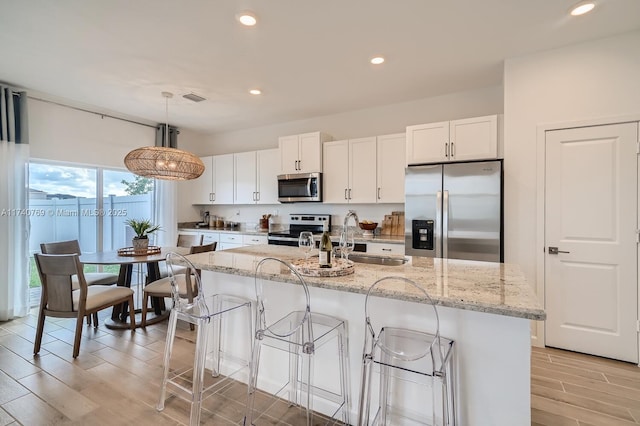 kitchen with white cabinetry, stainless steel appliances, sink, and hanging light fixtures