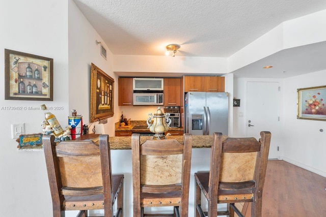 kitchen featuring appliances with stainless steel finishes, hardwood / wood-style floors, a kitchen breakfast bar, a textured ceiling, and kitchen peninsula