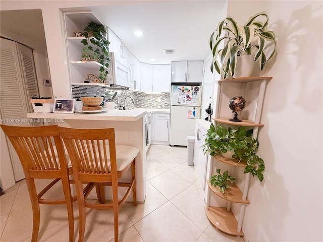 kitchen featuring a kitchen breakfast bar, kitchen peninsula, white appliances, decorative backsplash, and white cabinets