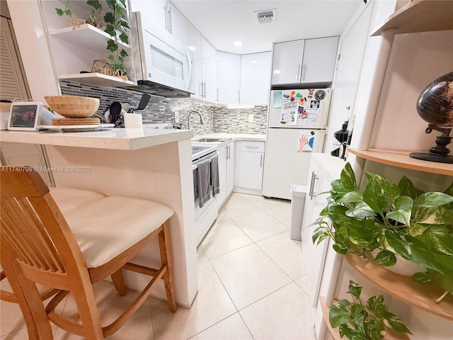 kitchen featuring white appliances, a kitchen breakfast bar, light tile patterned floors, and white cabinets