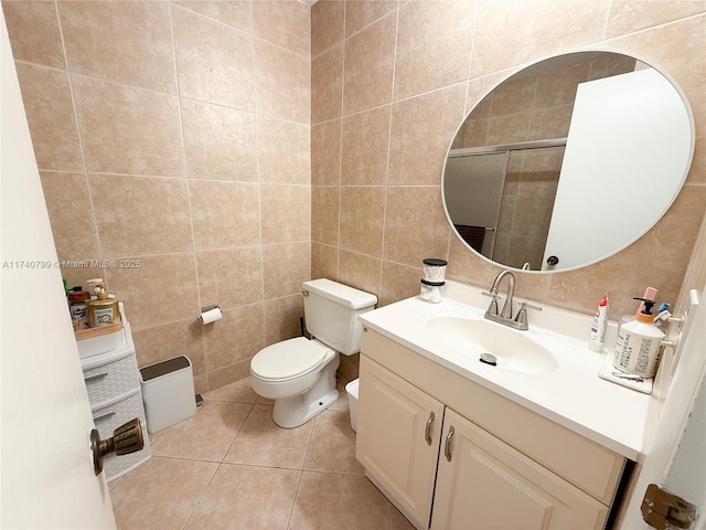 bathroom featuring a shower with shower door, tile walls, tile patterned flooring, vanity, and toilet