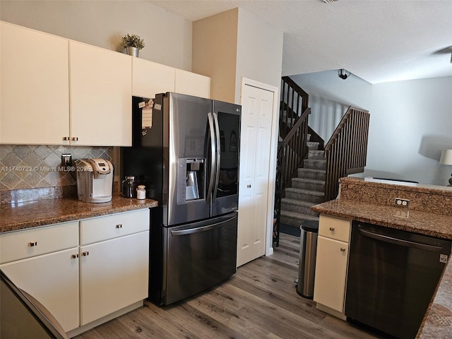 kitchen featuring white cabinets, stainless steel fridge, dark stone counters, and black dishwasher