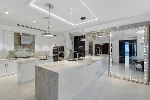 kitchen featuring a spacious island, wall chimney exhaust hood, sink, white cabinetry, and decorative light fixtures