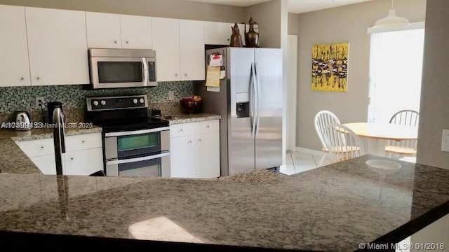 kitchen with stainless steel appliances, white cabinets, backsplash, and decorative light fixtures