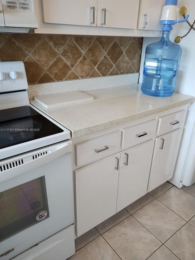 kitchen featuring light tile patterned floors, tasteful backsplash, light stone counters, white cabinets, and white electric stove