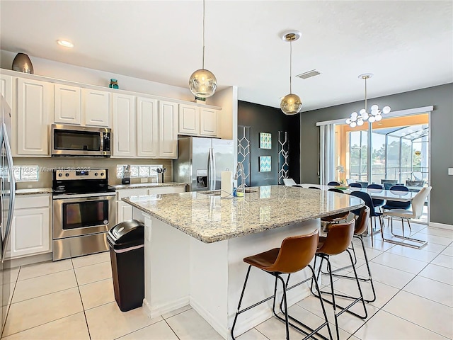 kitchen featuring decorative light fixtures, an island with sink, light tile patterned floors, stainless steel appliances, and light stone countertops