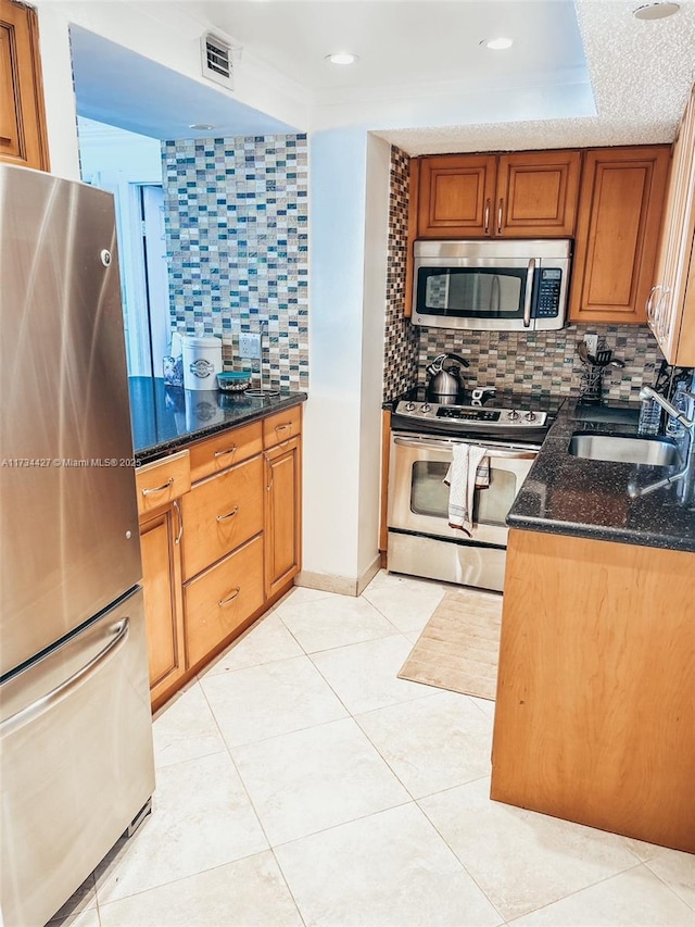 kitchen featuring appliances with stainless steel finishes, sink, dark stone counters, and a tray ceiling