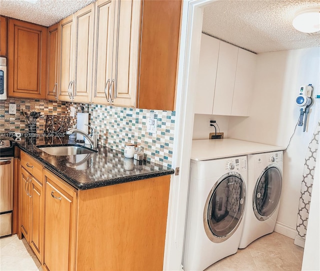 washroom with light tile patterned floors, washer and clothes dryer, a textured ceiling, and sink