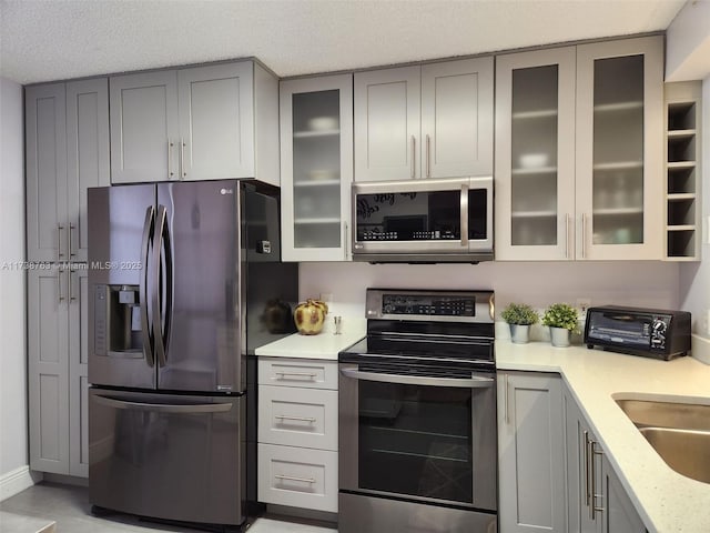 kitchen featuring sink, gray cabinets, stainless steel appliances, light stone counters, and a textured ceiling