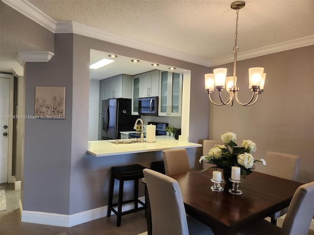 dining area featuring sink, crown molding, an inviting chandelier, a textured ceiling, and dark tile patterned floors