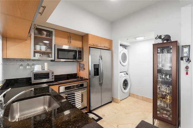 kitchen featuring stainless steel appliances, stacked washer and dryer, sink, and dark stone counters