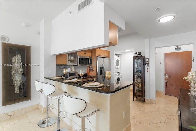 kitchen with a breakfast bar area, wine cooler, stacked washer / drying machine, kitchen peninsula, and stainless steel appliances