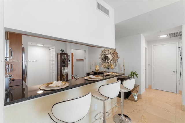 31 SE 5th St Unit 4018, Miami, FL 33131 - kitchen featuring light marble finish flooring, a peninsula, freestanding refrigerator, a breakfast bar, and dark stone countertops
