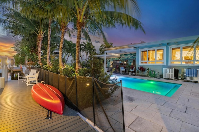 pool at dusk featuring a deck, a patio, central AC unit, and a fenced in pool