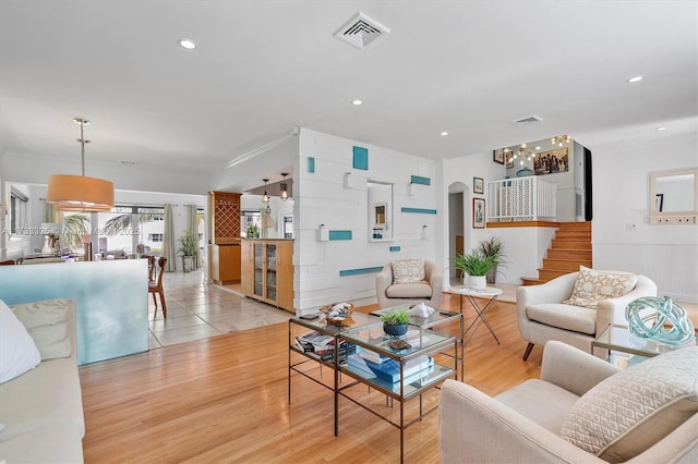 living room with light wood-style floors, arched walkways, visible vents, and stairway