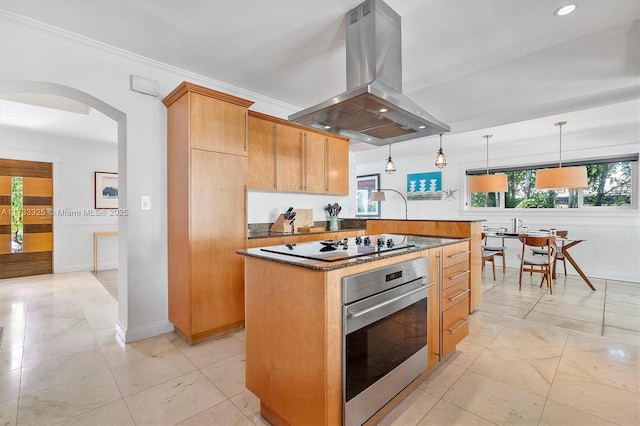 kitchen with arched walkways, dark countertops, decorative light fixtures, island exhaust hood, and stainless steel oven